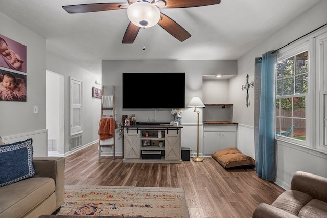 living area featuring ceiling fan, wainscoting, wood finished floors, and visible vents