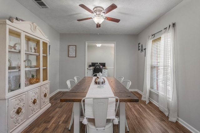 dining space featuring dark wood-style flooring, a ceiling fan, baseboards, and visible vents