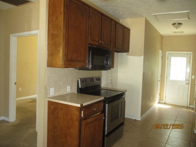 1902 6th Ct, Phenix City, AL 36867 - kitchen with stainless steel electric range oven, black microwave, light countertops, light tile patterned floors, and brown cabinets