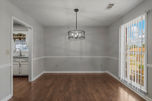 unfurnished dining area featuring a chandelier, visible vents, a wealth of natural light, and dark wood-type flooring