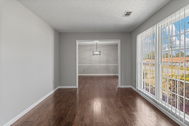 unfurnished dining area with a textured ceiling, visible vents, dark wood-style flooring, and baseboards