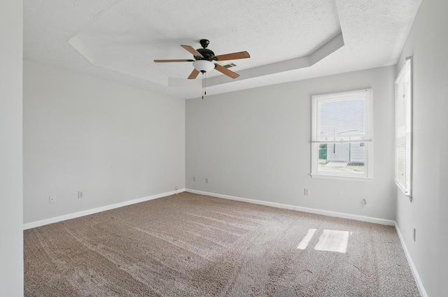 empty room with carpet floors, ceiling fan, baseboards, a raised ceiling, and a textured ceiling