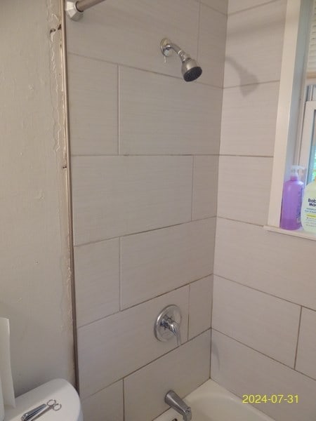 bathroom with toilet and tiled shower / bath