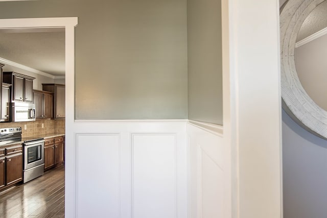 kitchen featuring crown molding, dark brown cabinets, wood-type flooring, and appliances with stainless steel finishes