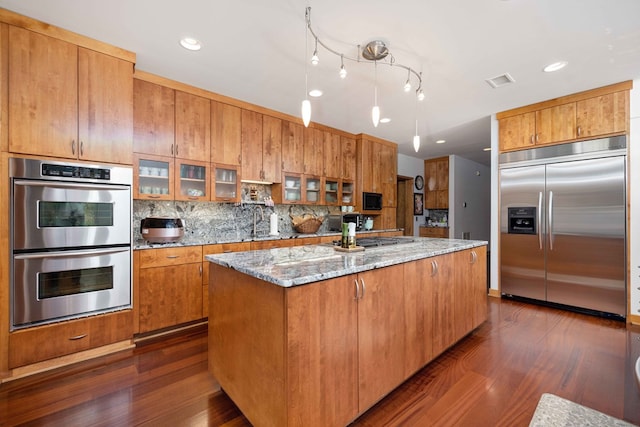 kitchen featuring light stone countertops, a center island, stainless steel appliances, and dark wood-type flooring