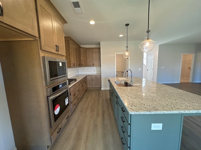 kitchen featuring light stone countertops, stainless steel appliances, hanging light fixtures, and an island with sink