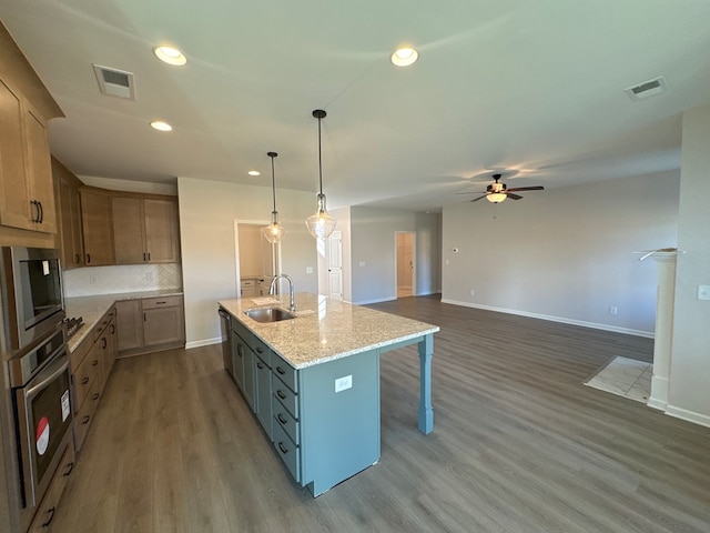 kitchen with light stone counters, stainless steel appliances, ceiling fan, a kitchen island with sink, and sink