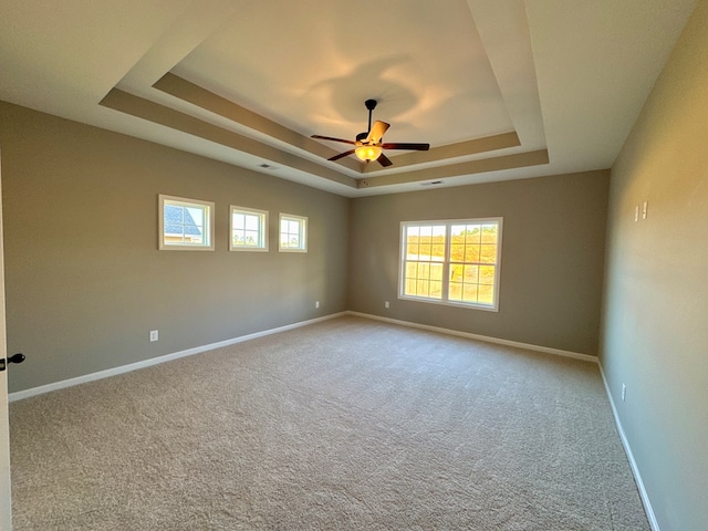 carpeted spare room featuring ceiling fan, plenty of natural light, and a tray ceiling