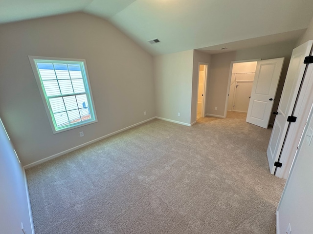 unfurnished bedroom featuring light carpet, a walk in closet, vaulted ceiling, and a closet