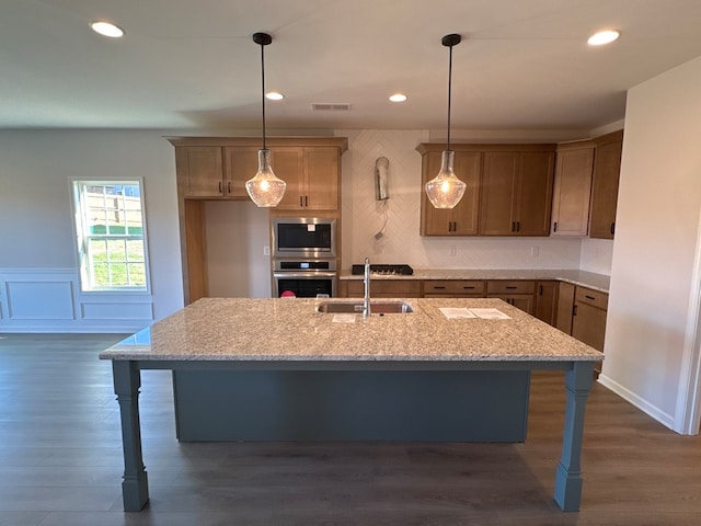 kitchen featuring light stone countertops, appliances with stainless steel finishes, a kitchen island with sink, sink, and decorative light fixtures