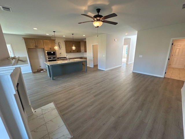 kitchen with sink, light stone counters, dark hardwood / wood-style flooring, pendant lighting, and a kitchen island with sink