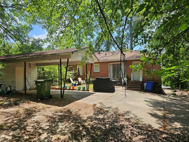 back of property featuring a carport, concrete driveway, a patio area, and brick siding