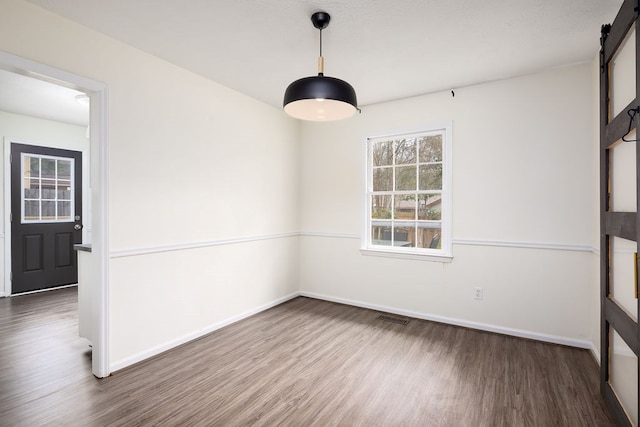 empty room featuring a barn door, baseboards, visible vents, and wood finished floors