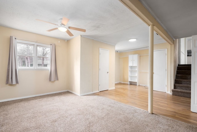 carpeted empty room featuring a textured ceiling, wood finished floors, baseboards, ceiling fan, and stairs