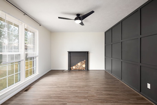 unfurnished living room with a decorative wall, wood finished floors, visible vents, and ceiling fan