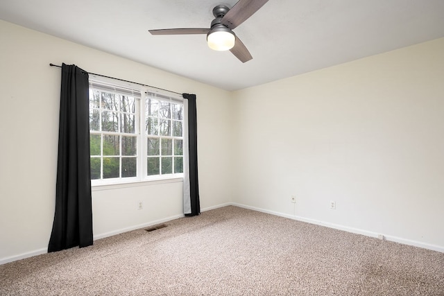 carpeted spare room featuring baseboards, visible vents, and ceiling fan