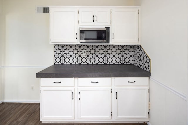 kitchen with visible vents, dark wood finished floors, decorative backsplash, white cabinets, and stainless steel microwave