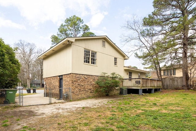 rear view of house with a gate, fence, a deck, a lawn, and brick siding