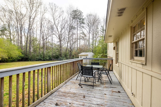 wooden terrace featuring visible vents, an outdoor structure, outdoor dining space, and a yard