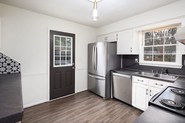 kitchen with a wainscoted wall, a sink, appliances with stainless steel finishes, white cabinetry, and dark countertops