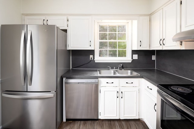 kitchen featuring dark countertops, dark wood-type flooring, appliances with stainless steel finishes, white cabinets, and a sink