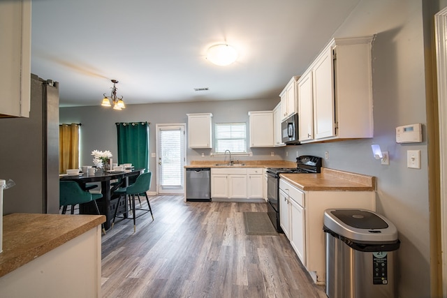 kitchen with dark wood-type flooring, black appliances, sink, hanging light fixtures, and white cabinetry