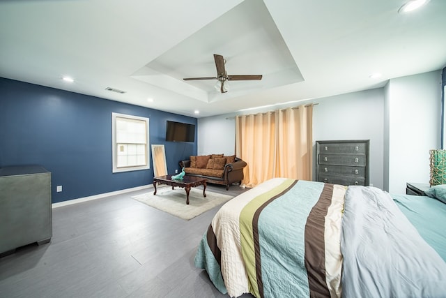 bedroom with hardwood / wood-style flooring, a raised ceiling, and ceiling fan