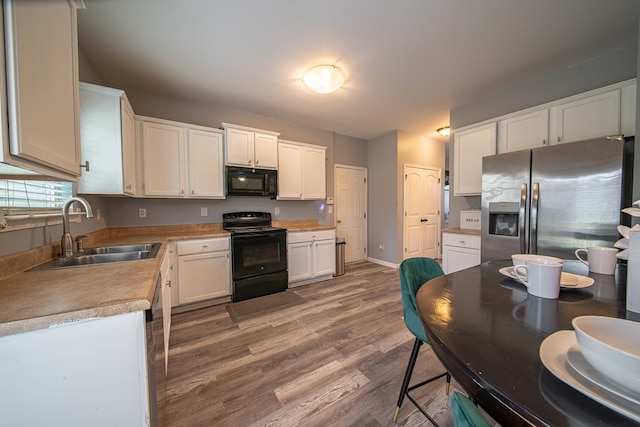 kitchen featuring hardwood / wood-style floors, white cabinetry, sink, and black appliances