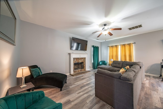 living room with a tiled fireplace, ceiling fan, and wood-type flooring