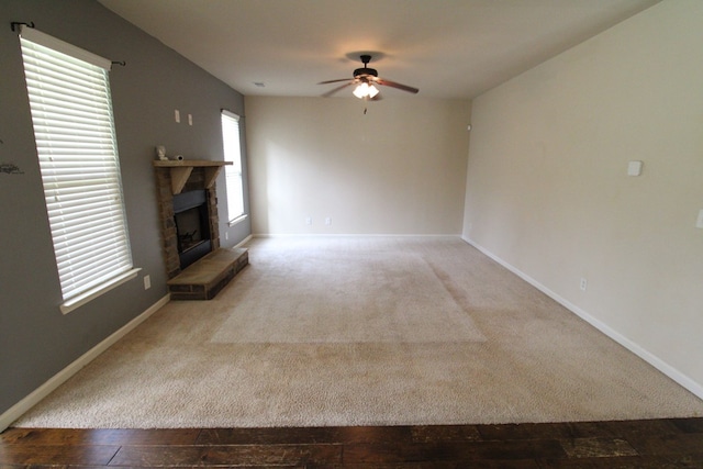 unfurnished living room with a fireplace with raised hearth, baseboards, carpet, and ceiling fan