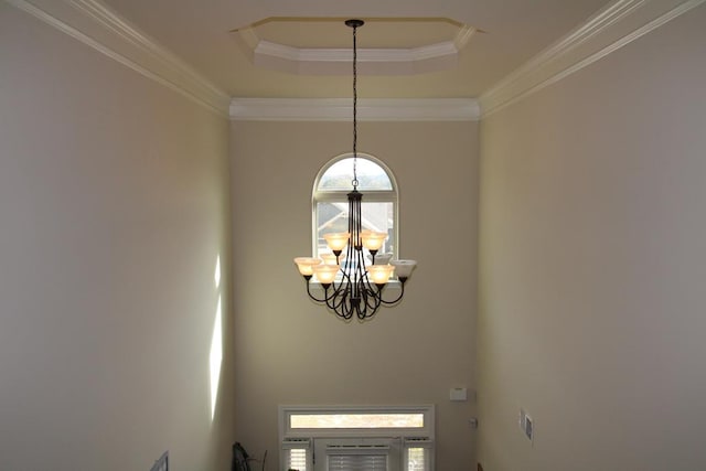 entryway with a raised ceiling, a chandelier, and ornamental molding