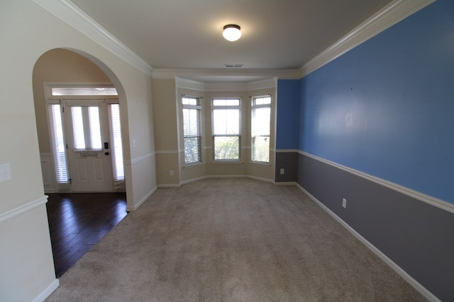 carpeted foyer entrance with baseboards, arched walkways, visible vents, and ornamental molding