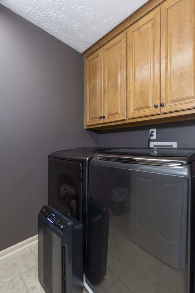 laundry room with washing machine and dryer, a textured ceiling, and cabinets