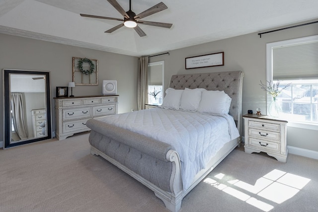 bedroom with ceiling fan, light colored carpet, multiple windows, and a raised ceiling