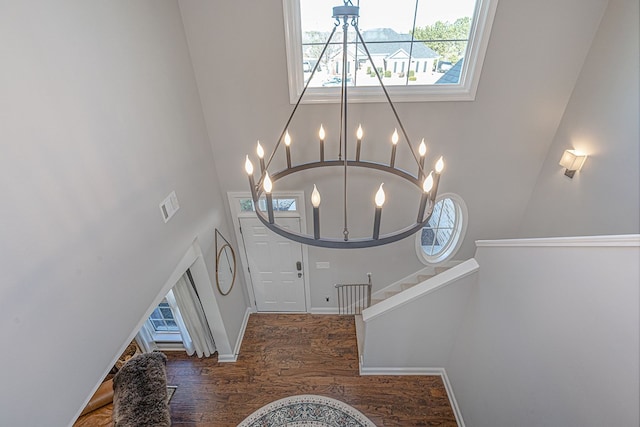 entryway featuring dark wood-type flooring, a towering ceiling, and a notable chandelier