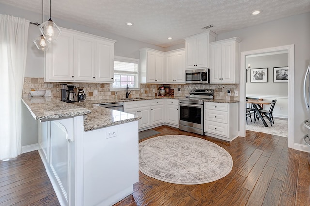 kitchen featuring dark hardwood / wood-style floors, kitchen peninsula, white cabinetry, hanging light fixtures, and stainless steel appliances