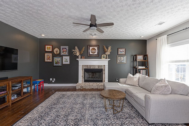 living room with a textured ceiling, a brick fireplace, dark wood-type flooring, and ceiling fan