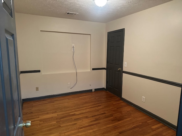 spare room with dark wood-style flooring, a textured ceiling, visible vents, and baseboards
