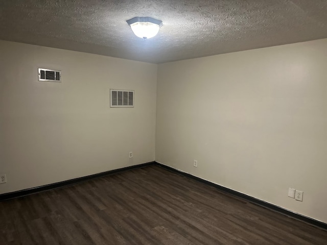 unfurnished room featuring baseboards, dark wood-type flooring, a textured ceiling, and visible vents