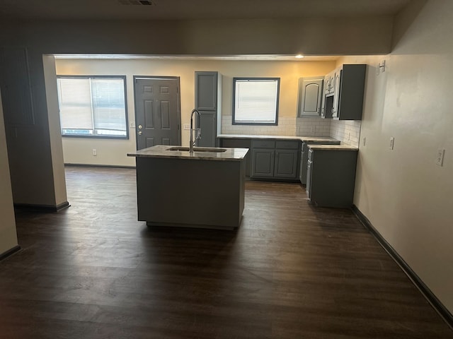 kitchen with dark wood-type flooring, a sink, gray cabinets, and a kitchen island with sink