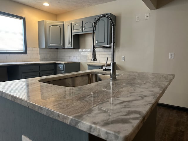 kitchen featuring dark wood-style flooring, a textured ceiling, gray cabinets, a sink, and backsplash