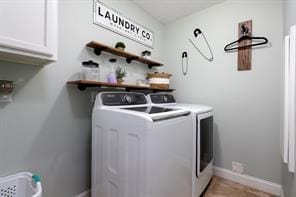 clothes washing area with washer and clothes dryer, cabinet space, and baseboards