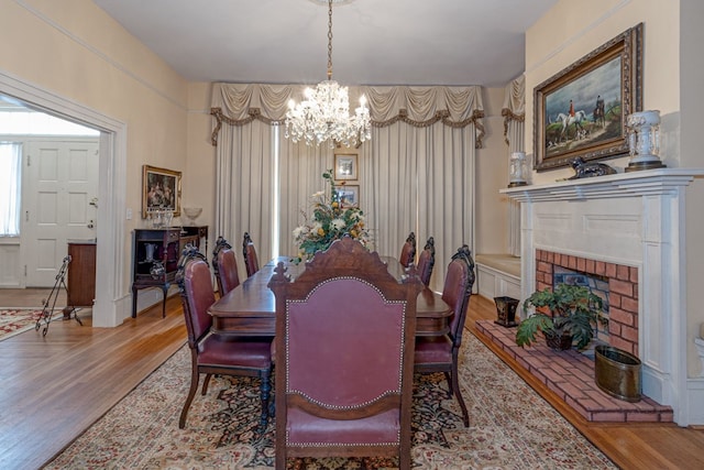 dining space featuring a notable chandelier, wood-type flooring, and a brick fireplace