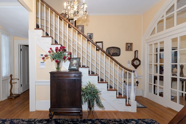 stairs featuring french doors, wood-type flooring, ornamental molding, and an inviting chandelier