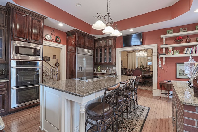 kitchen with built in appliances, light wood-type flooring, an island with sink, and a chandelier