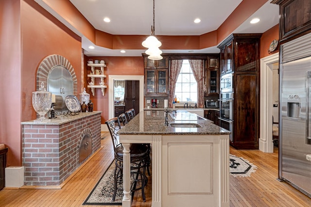 kitchen with built in appliances, dark brown cabinets, a kitchen bar, and dark stone counters