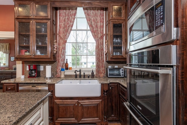 kitchen featuring a healthy amount of sunlight, light stone countertops, sink, and appliances with stainless steel finishes