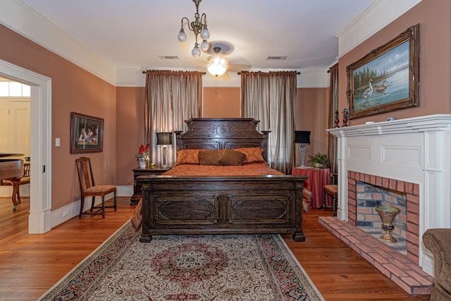 bedroom featuring an inviting chandelier, ornamental molding, a fireplace, and light hardwood / wood-style flooring