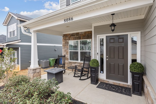 entrance to property featuring stone siding, covered porch, and central air condition unit