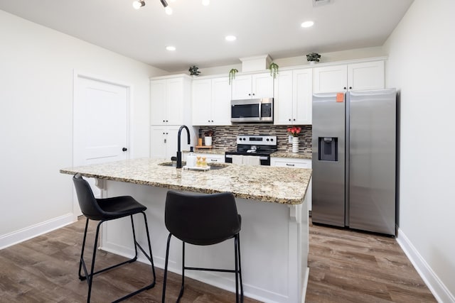 kitchen featuring white cabinets, dark wood-style floors, an island with sink, a sink, and appliances with stainless steel finishes